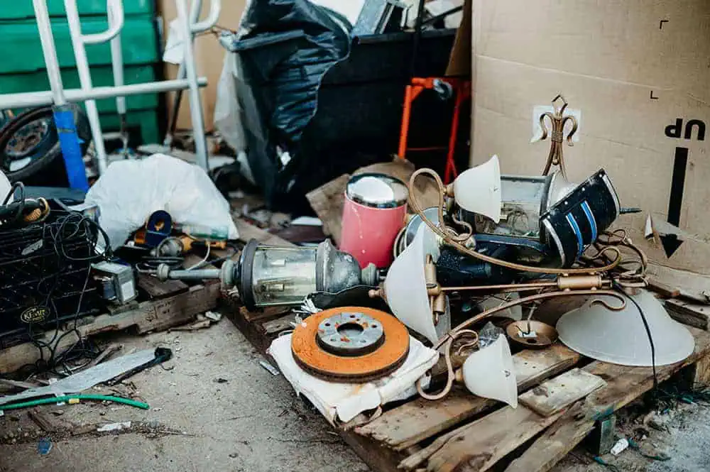 A pile of discarded household items and broken light fixtures on wooden pallets near cardboard and garbage bags outdoors.