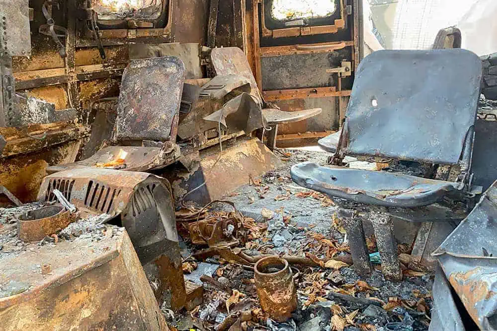 Burned metal chairs and debris inside a destroyed vehicle interior