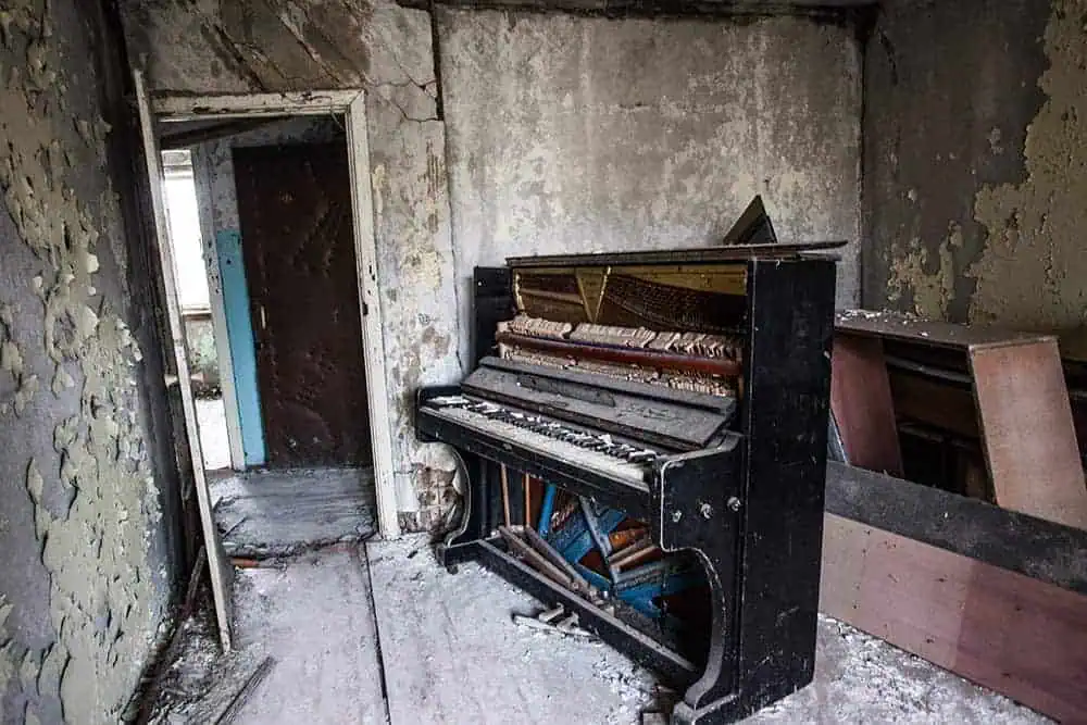 Abandoned upright piano with missing keys and exposed strings in a decaying, paint-peeling room.