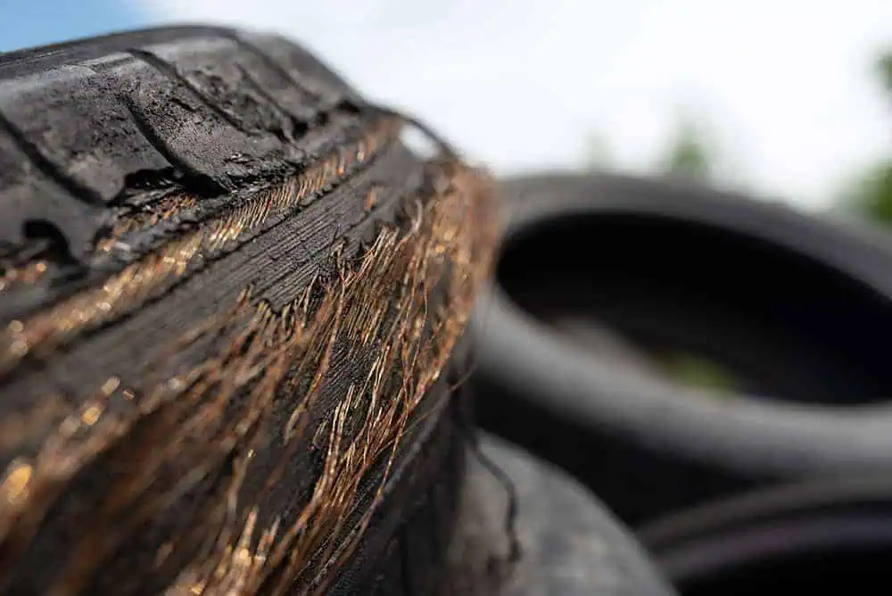 Close-up of a shredded tire exposing frayed metal wires with other old tires in the background